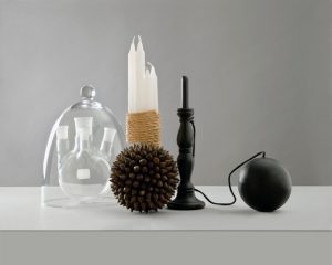 Photographie proposée par d'Anne Veaute pour illustrer le confinement : objets posés sur une table blanche : un bilboquet, une cloche en verre, un bouquet de bougies